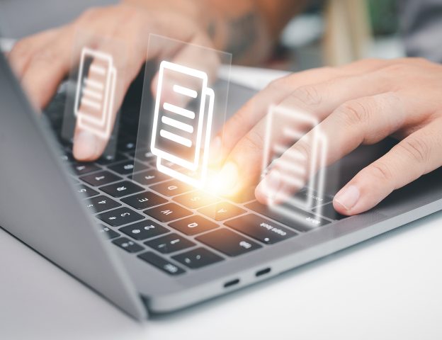 Fingers typing on a laptop with document icons floating above
