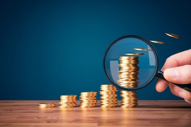 Hand with magnifying glass focused on coins fly away