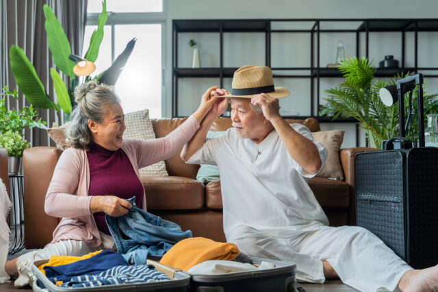 Senior couple sitting on the floor of a family room with luggage packing for a trip