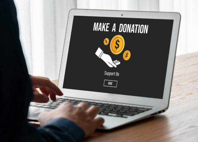 View of a laptop on a desk and the screen reads make a donation, support us, give